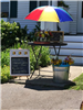 Flower stand with a red, yellow, and blue umbrella and a sign displaying prices for mason jars and bouquets