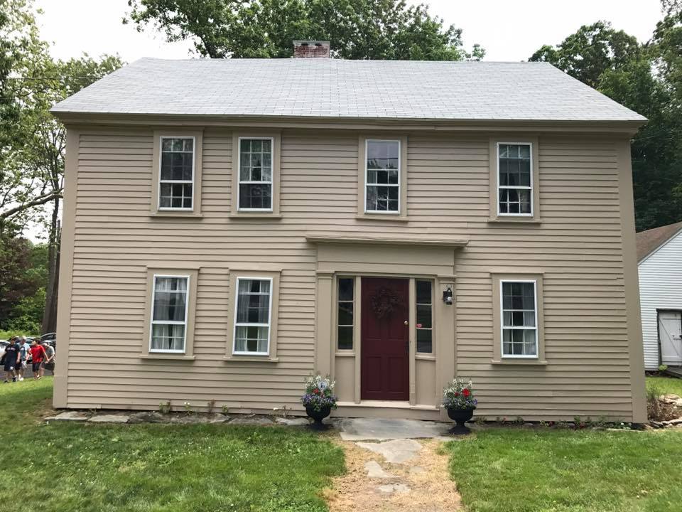 Tan home with two pots of flowers in the front and people walking on the side of the house