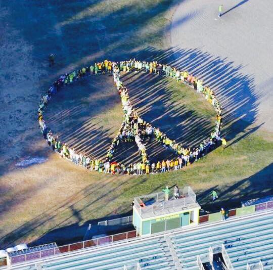 People standing in the form of a peace symbol near bleachers